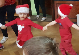 dzieci tańczą w czerwonych strojach i czapkach mikołajkowych